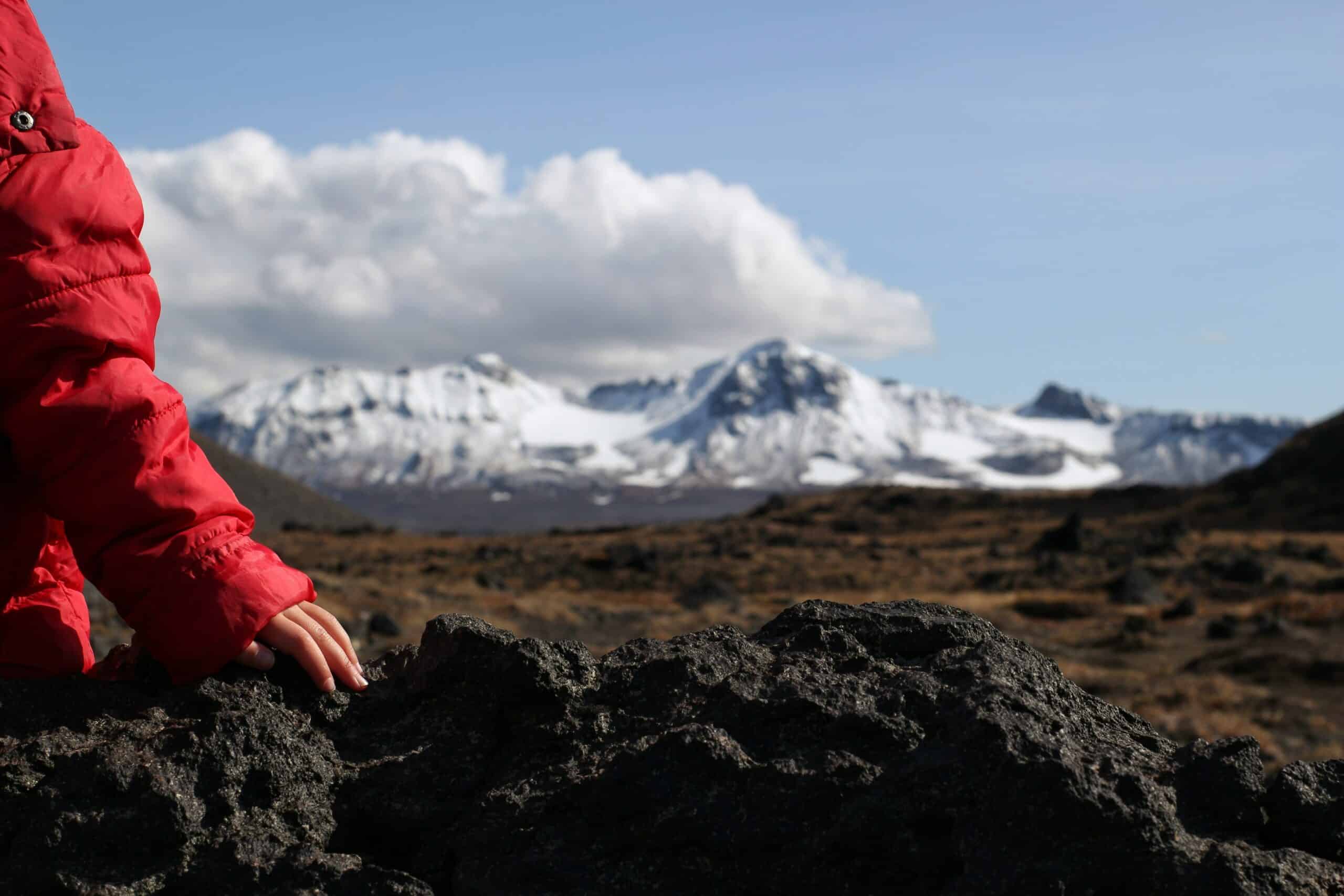 person in red jacket sitting on rock
